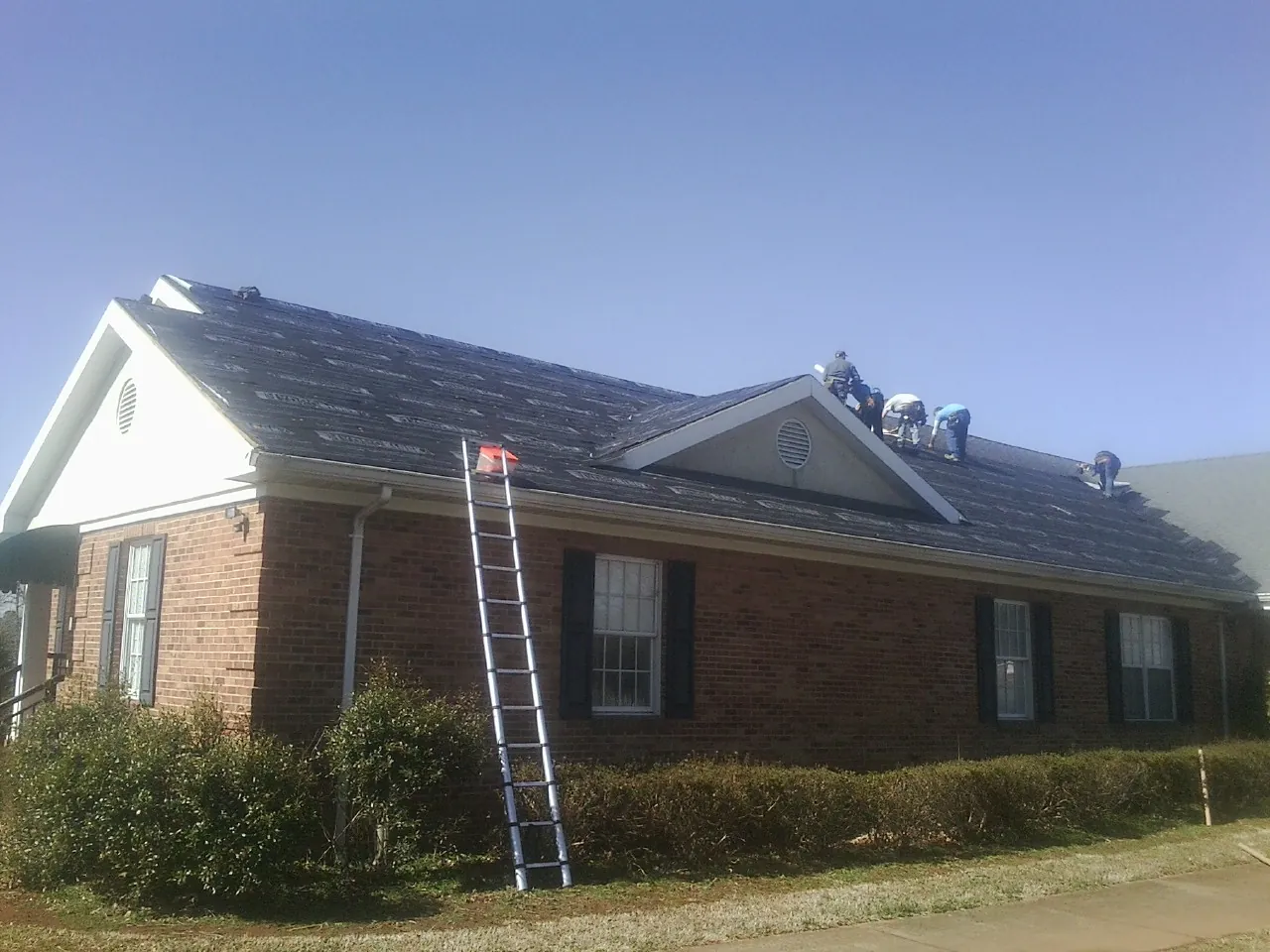 Crew tearing shingles off a brick ranch roof with a ladder set — Metal Roof Repair work by our crew in Greenbrae