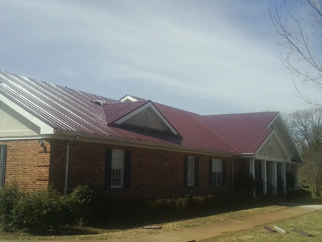Red metal roof with gabled entries on a long brick building, from a Hail Damage Roof Repair job in Greenbrae