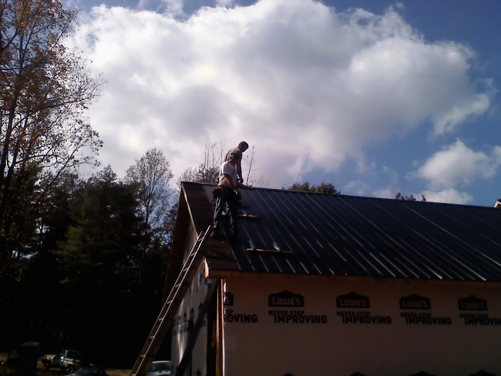 Roofer fastening dark metal panels high against a cloudy sky, from a Roof Inspection job in Greenbrae